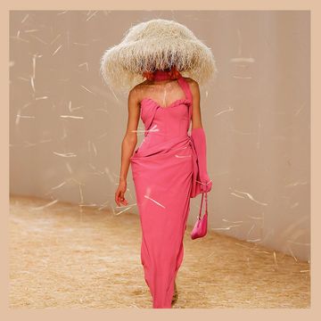 on the left is a model draped in a coral slinky dress wearing a large hat that covers her head that looks like a beige sea urchin and on the right is a pendant light that look just like the hat as a beige sea urchin