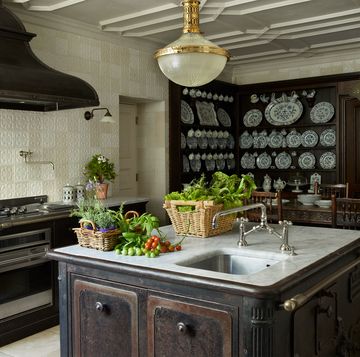 kitchen with square dark cast iron island with small sink and white marble top and oval light fixture overhead and a large old looking oven with a wide hood and the walls covered in a pale creamish yellow linen paper