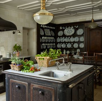 kitchen with square dark cast iron island with small sink and white marble top and oval light fixture overhead and a large old looking oven with a wide hood and the walls covered in a pale creamish yellow linen paper
