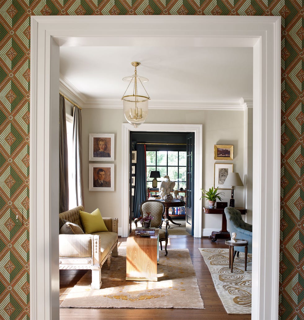 entryway arch with green patterned paper looking into a living room with sofa rugs and blue chair and further into another doorway into a blue room with pedestal table at center