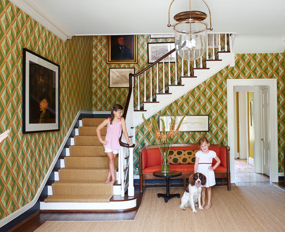 dramatic staircase lined with yellow and greenish gold pattern paper and two little girls standing by it with a dog