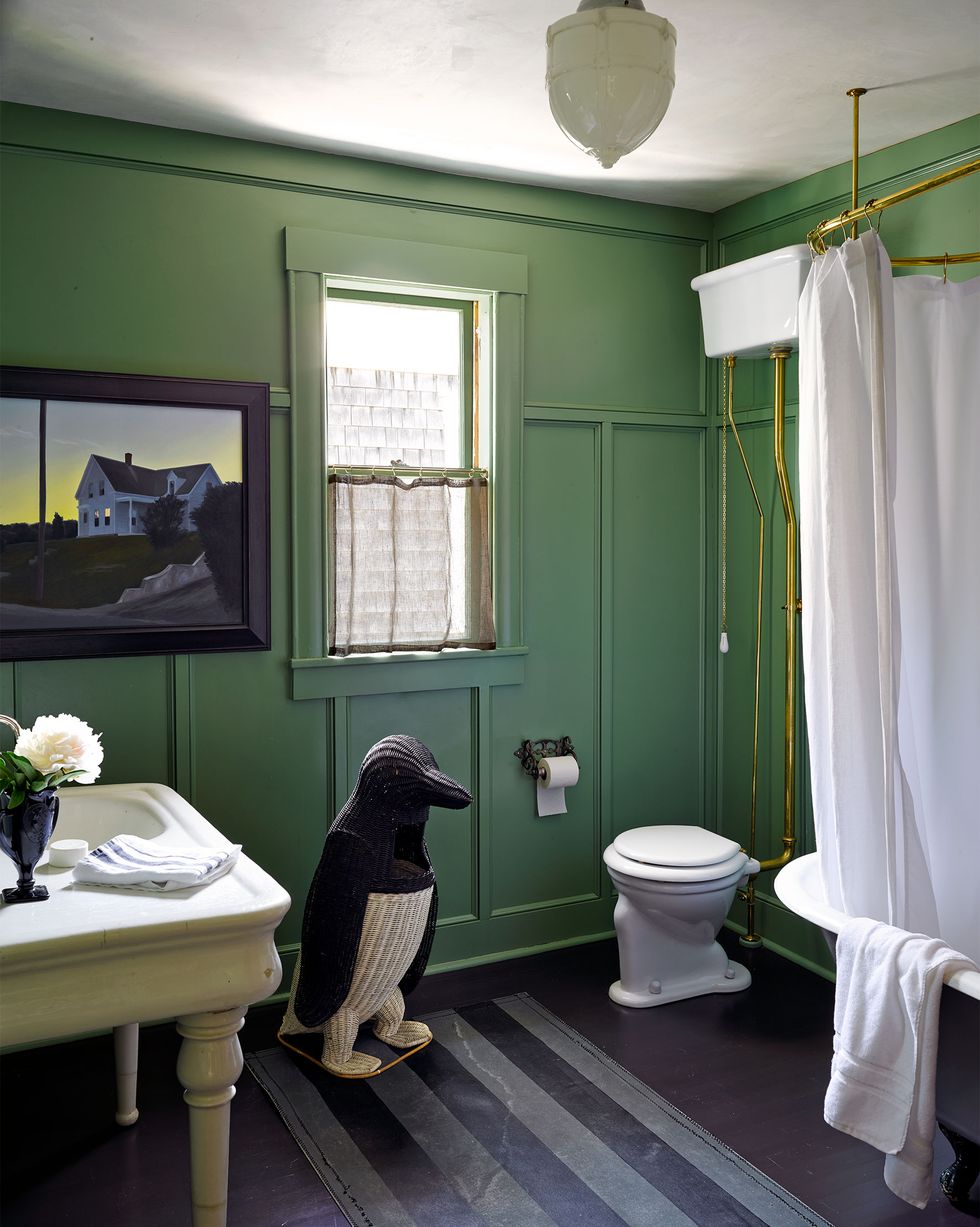 green bathroom with a large knit penguin and striped runner and a standalone tub with curtain and old timey pull string toilet tank