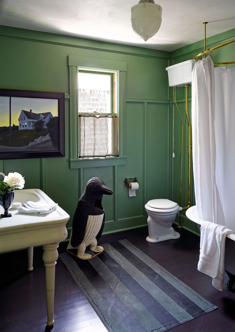 green bathroom with a large knit penguin and striped runner and a standalone tub with curtain and old timey pull string toilet tank