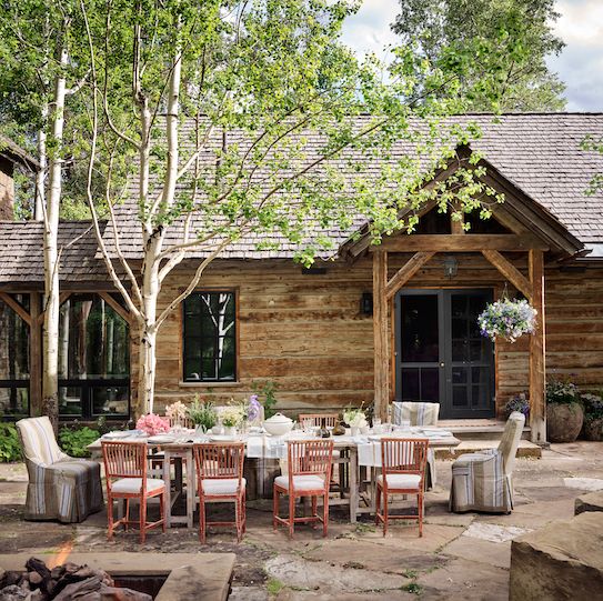 jeffrey bilhuber dining chairs on a stone patio in front of a rustic log house