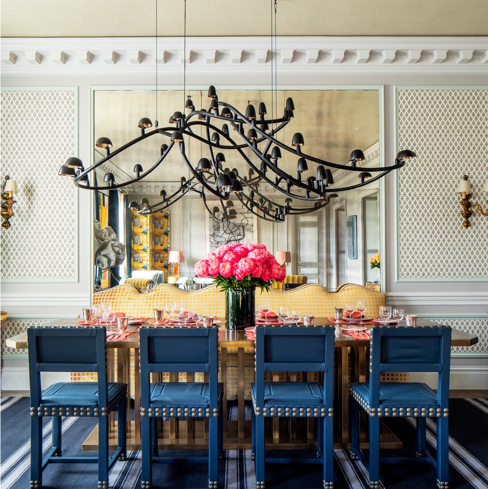 blue dining chairs surround a dining table with orange place settings and pink peonies