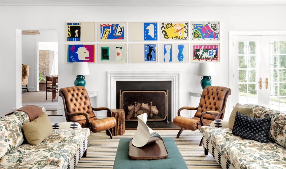 james huniford cottage in westchester county, new york featuring a fireplace with a brass screen, leather armchairs, and wall prints on the walls
