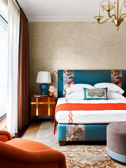 a beige primary bedroom with a blue patterned bed frame and sheets with orange accents
