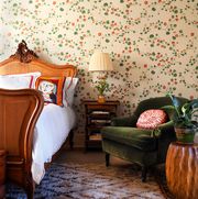 bedroom with viney green and red flowered wallpaper a sleigh bed and a green velvet upholstered chair to the right