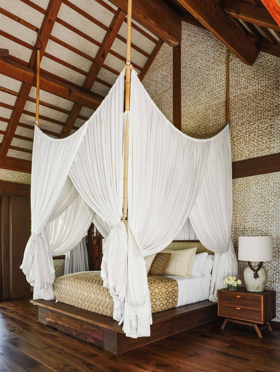 a bedroom with a draped canopy bed area wooden floors and a nearby wood side table