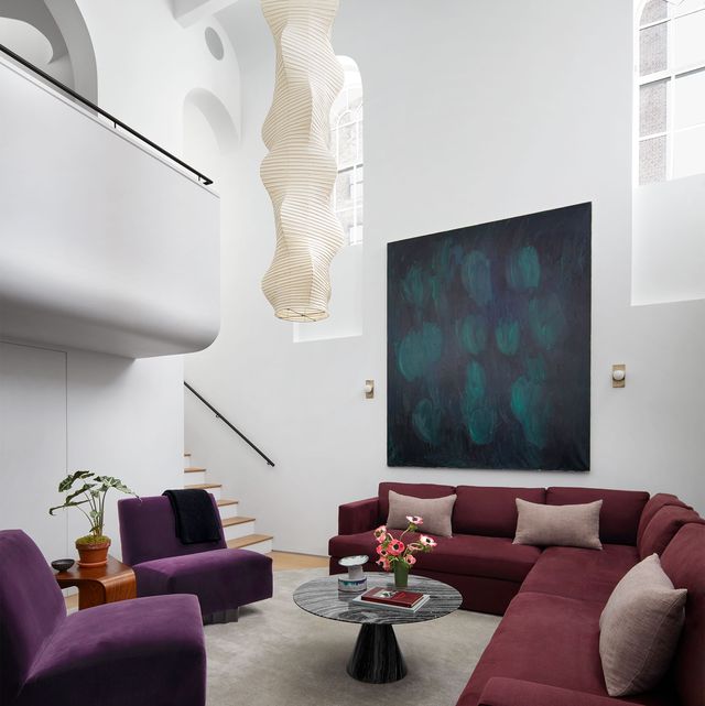 living area with high ceilings wraparound sofa in dark burgundy with armless chairs in complimentary dark purple velvet and a low coffee table with triangular pedestal and large handing pendant from ceiling