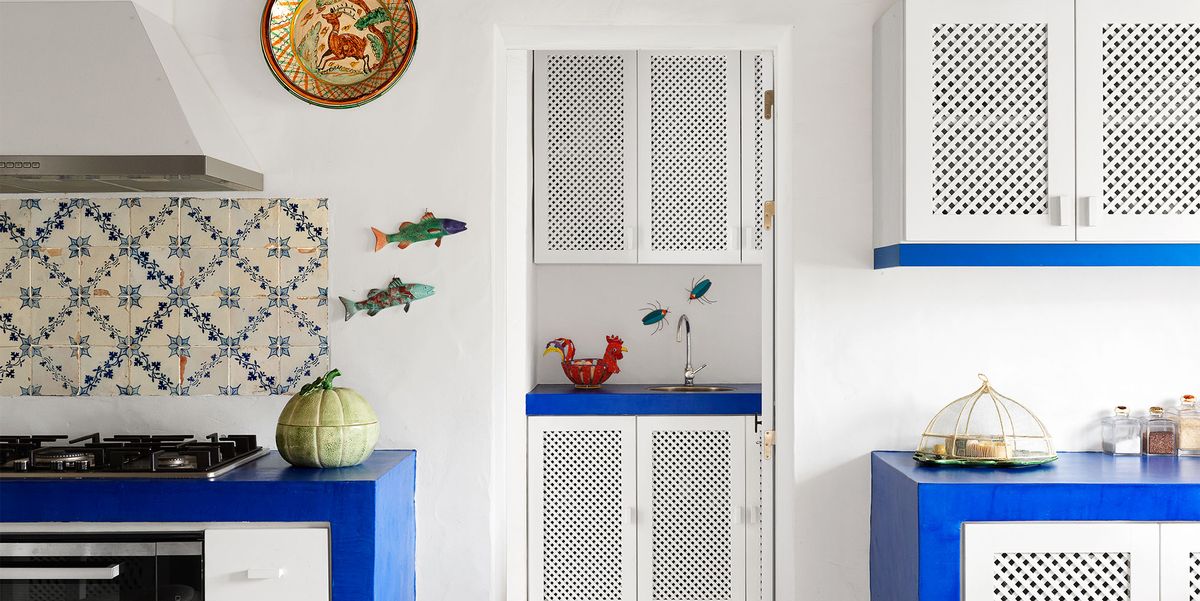 a kitchen with white walls and cabinets accented with deep blue counters, blue and white tiles, ceramic fish and portuguese plates adorn the walls, four ceramic pitchers in the shape of chickens top a cabinet