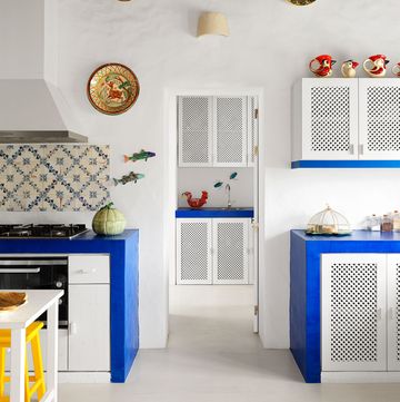 a kitchen with white walls and cabinets accented with deep blue counters, blue and white tiles, ceramic fish and portuguese plates adorn the walls, four ceramic pitchers in the shape of chickens top a cabinet