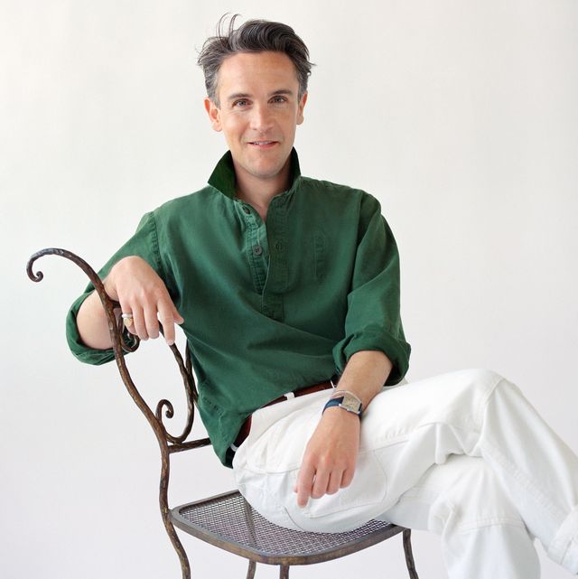 designer in green shirt and white pants sitting on an iron garden chair