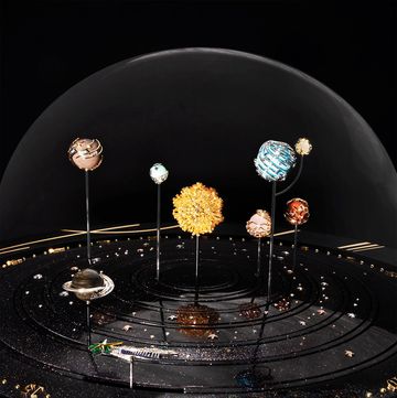 a glass enclosed solar system made up of jewels on pins in a black starry base with knobs a the bottom