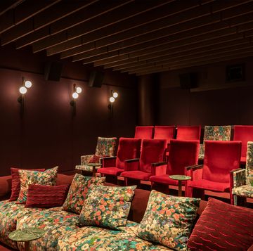 a tiered media room with red velvet and floral seating and small tables and wall lights