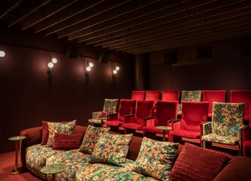 a tiered media room with red velvet and floral seating and small tables and wall lights