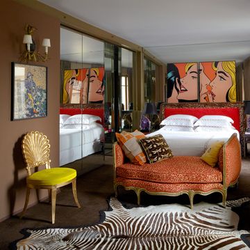 long bedroom with a salmon sofa and then the bed behind it and a large pop art painting on the wall behind the bed and a wall of curtains on the right and mirrored doors on the left