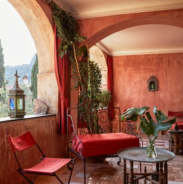 iron settee and chair with red cushions and brick floors and a small round table on a enclosed terrace like room with red curtains