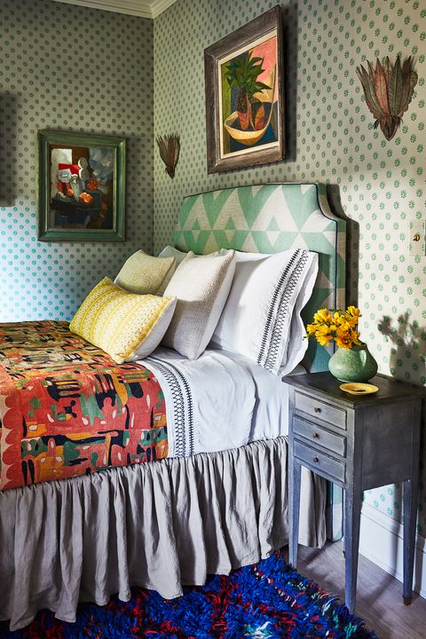 small bed with green patterned upholstered headboard against a wall also with green highlights and hanging art