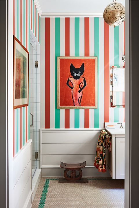 small guest bathroom with white fixtures and striped wallpaper and art hanging on the wall