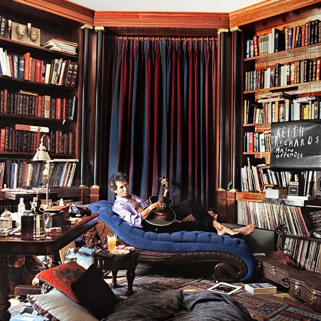 rolling stones keith richards holding a guitar on a chaise longue in a massive library room