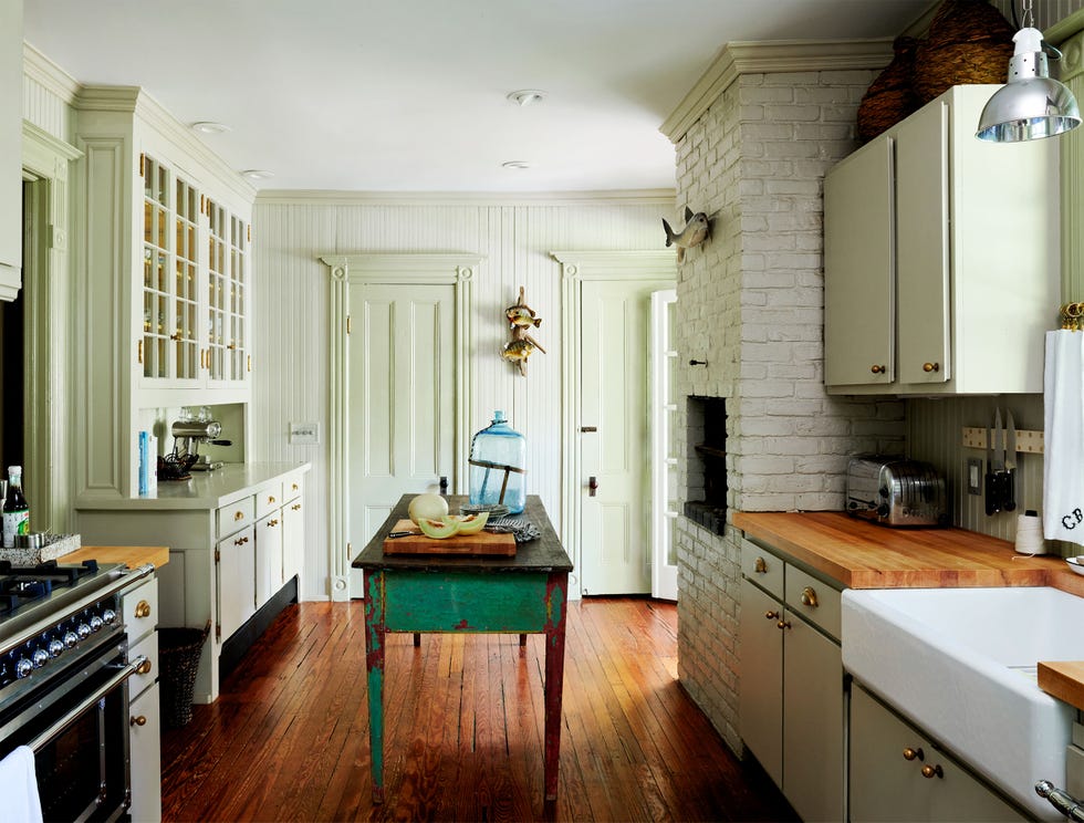 farmhouse kitchen with a small green painted antique table at center white brick walls and original white cabinetry