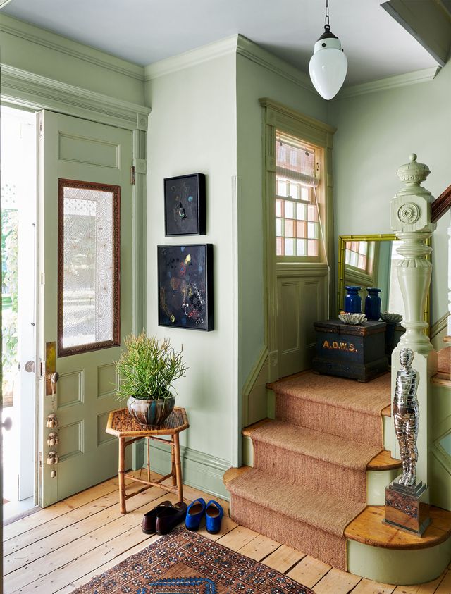 a sage colored entryway with carpeted stairs two artworks and a pendant light above
