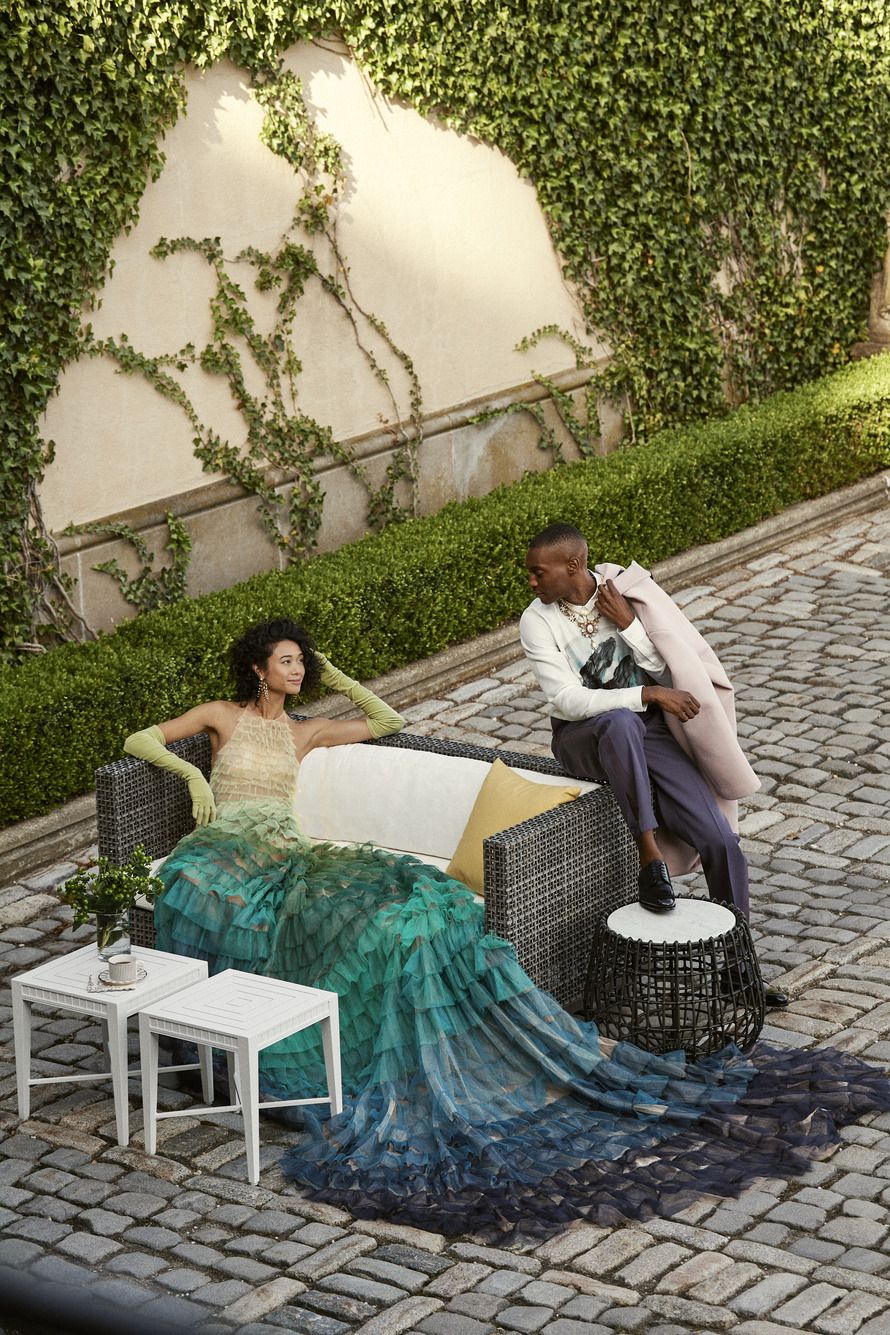 into the glamour garden janus et cie hoffman cocktail tables, boxwood smoke two seat sofa, capri butterfly pillow, and vino side table fashion, from left gown by christian dior shirt, pants, and shoes by dior homme coat by prada