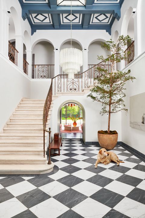entryway with a dramatic black and white tiled floor and a white stone stairway going up and a tree in a stone planter by an arch and a very cute golden retriever lying out relaxed on the tile floor