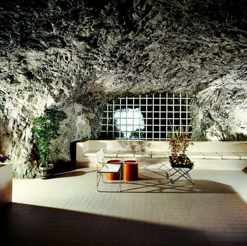 cave room with spare furniture with a very long white banquette and some red stools as highlight