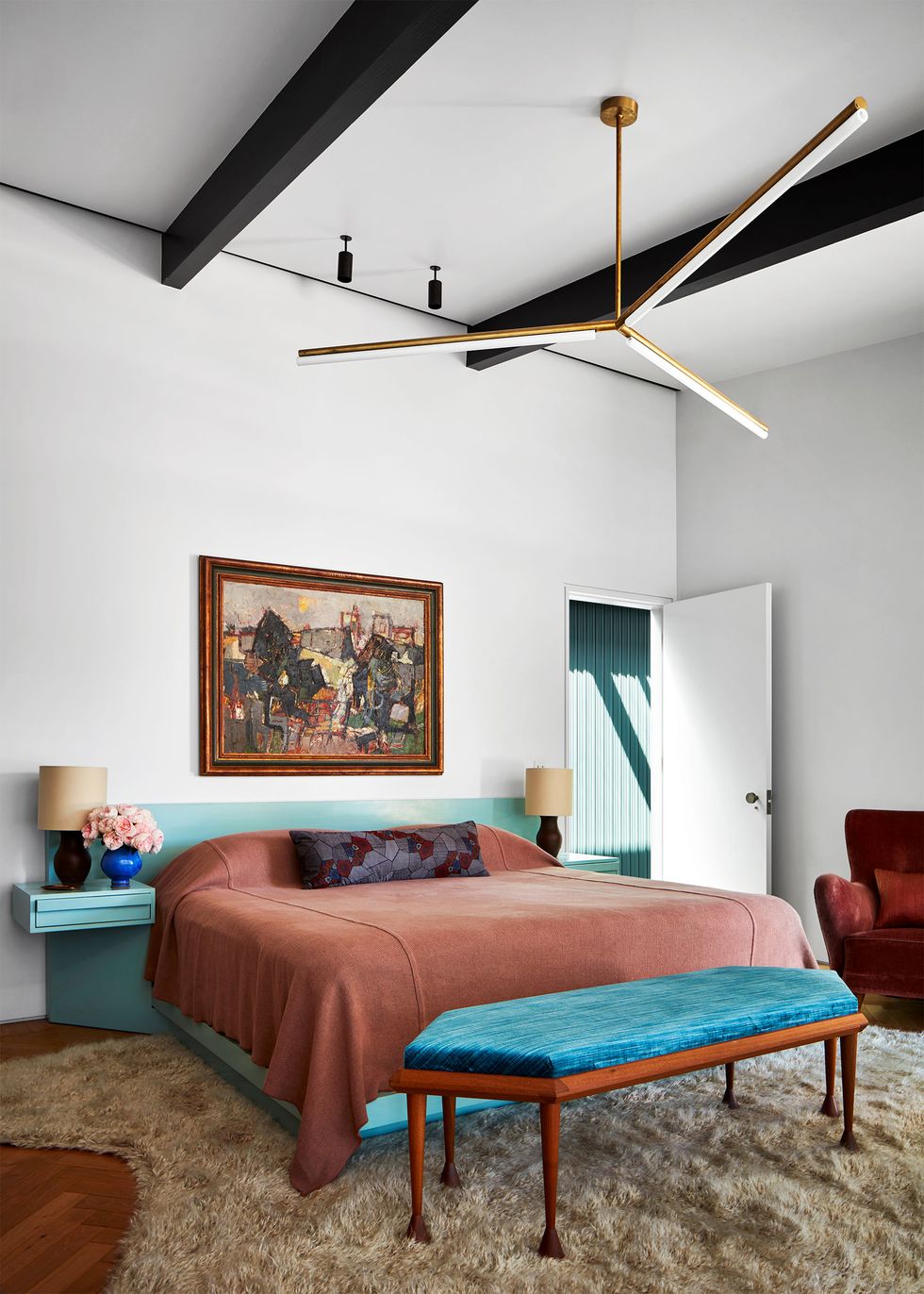a primary bedroom has a light aqua platform bed with attached headboard and side tables with lamps, a bench with wood base and deep turquoise fabric seat, a painting above bed, and a beige shag rug