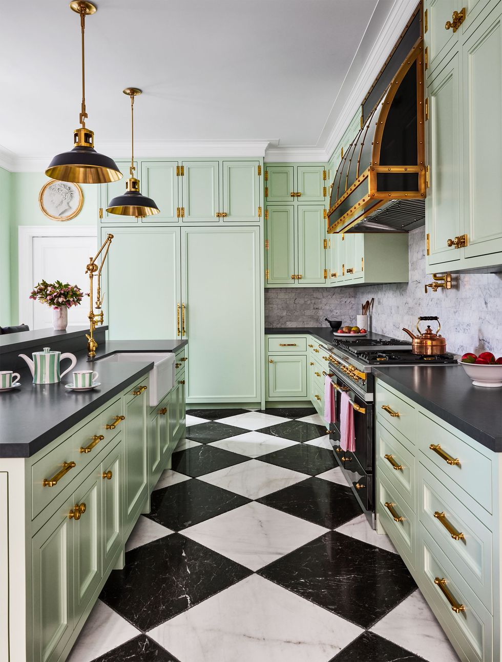light green modern kitchen with black countertops and black and white checked diamond flooring and bronze and black finish hardware including the pendants over the island