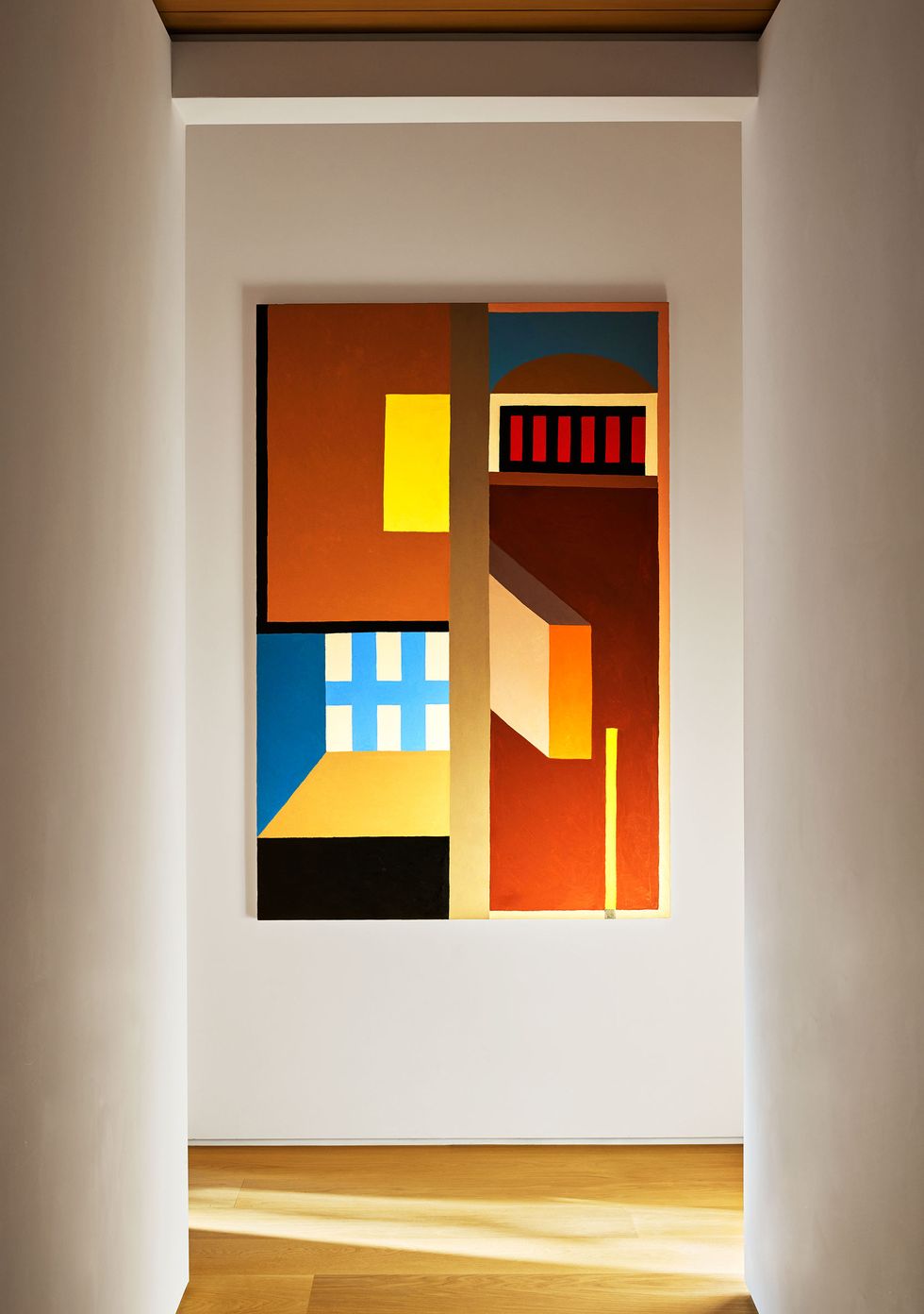 in a hallway with white walls and a wood floor hangs a painting with squares and rectangles in terracotta, blue, yellow, black, orange, and yellow