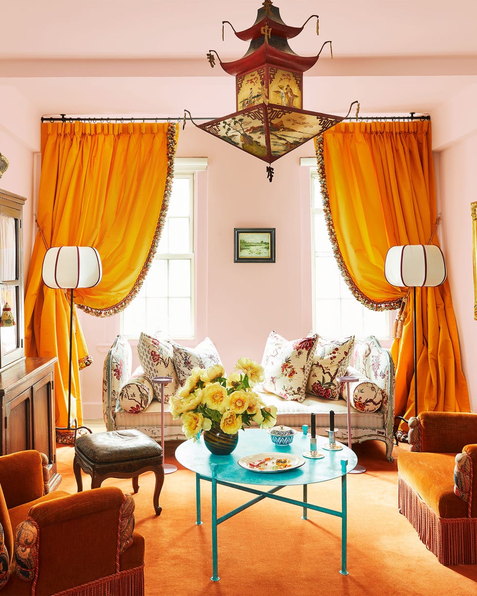 Rebecca Gardner - ELLE DECOR a bird and flower patterned daybed is behind saffron draped curtains and two floor lamps, in foreground is a turquoise cocktail table, two saffron velvet antique chairs, a cabinet, a pagoda pendant, and artworks