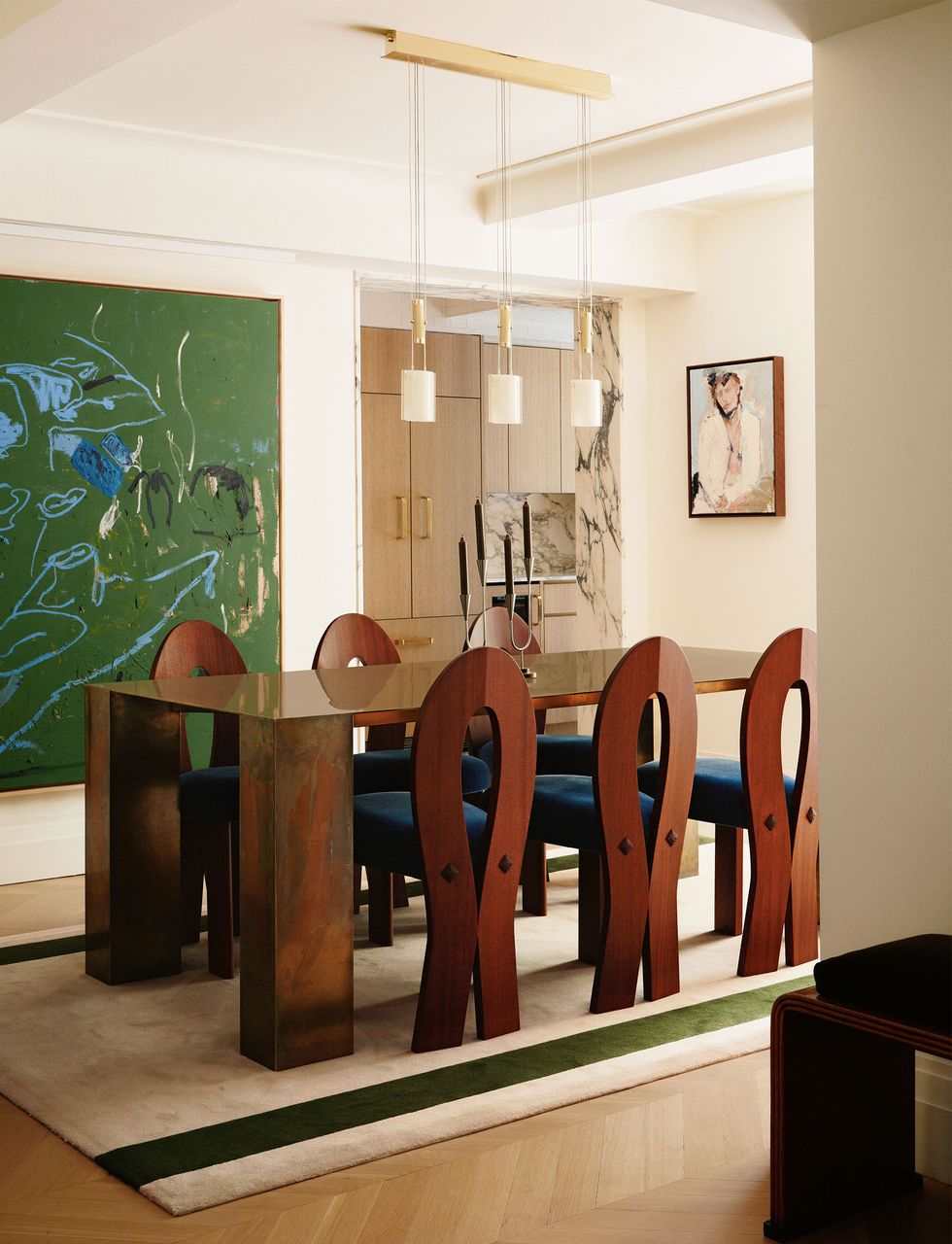 a dining room table has rectangular pillar legs and glazed top, six dark wood chairs with tear drop shaped backs and navy cushioned seats, a trio of pendants, large primarily green painting, light rug with two green stripes