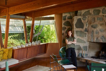 a person standing in an open room with a large stone fireplace on the right and wood beams and floors and window frames and furnture