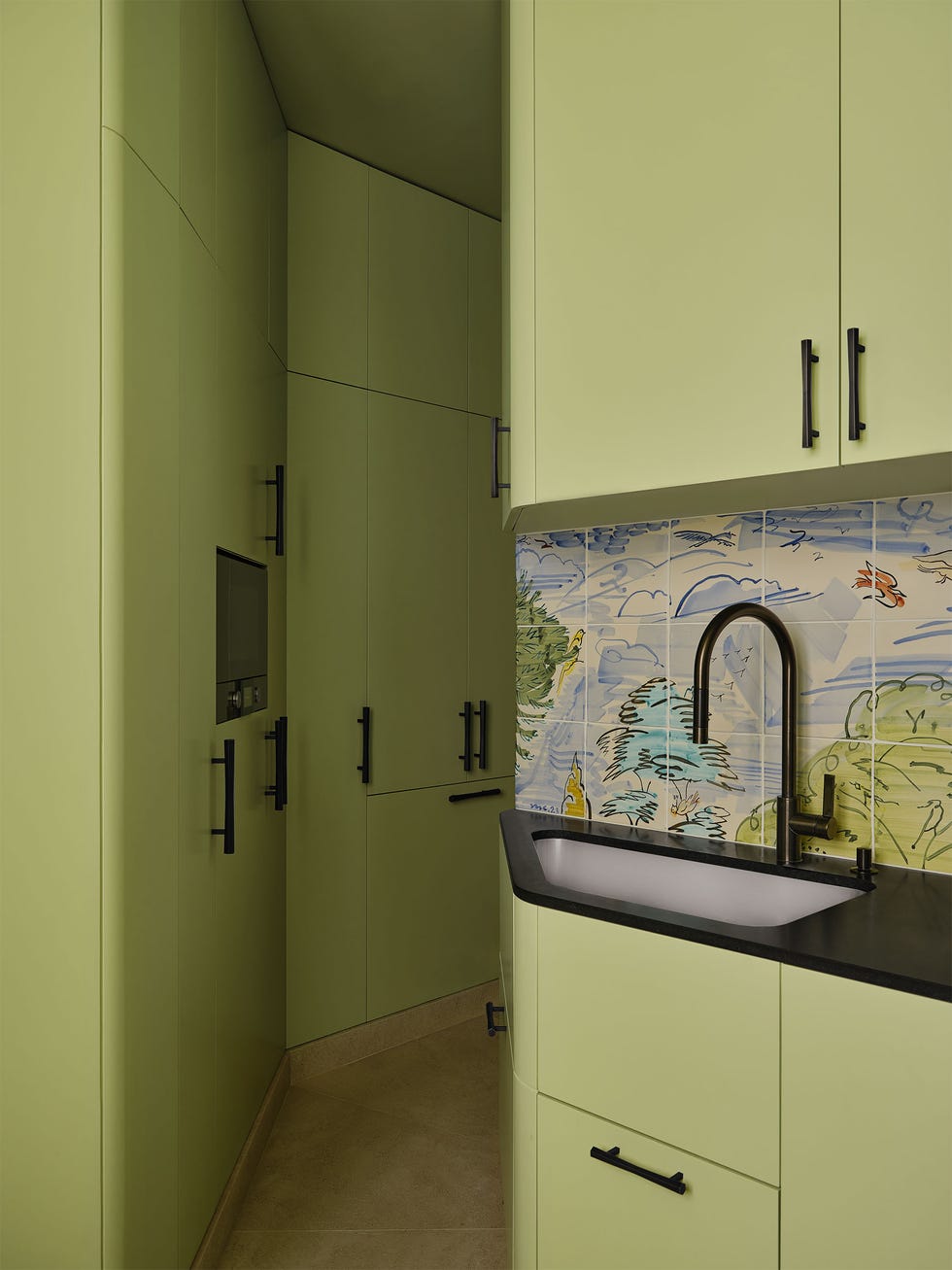 Pierre Yovanovitch - ELLE DECOR a kitchen has light avocado colored cabinets with black pulls along a corridor and above and below a sink set in a black coun