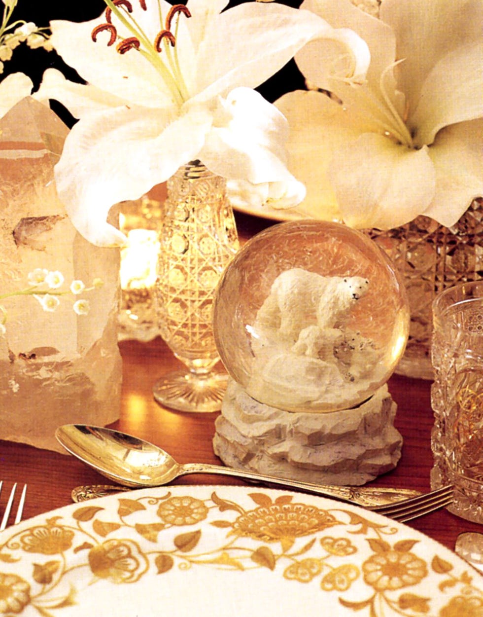 a table with a vase of flowers and a candle and a snowglobe with a polar bear in it