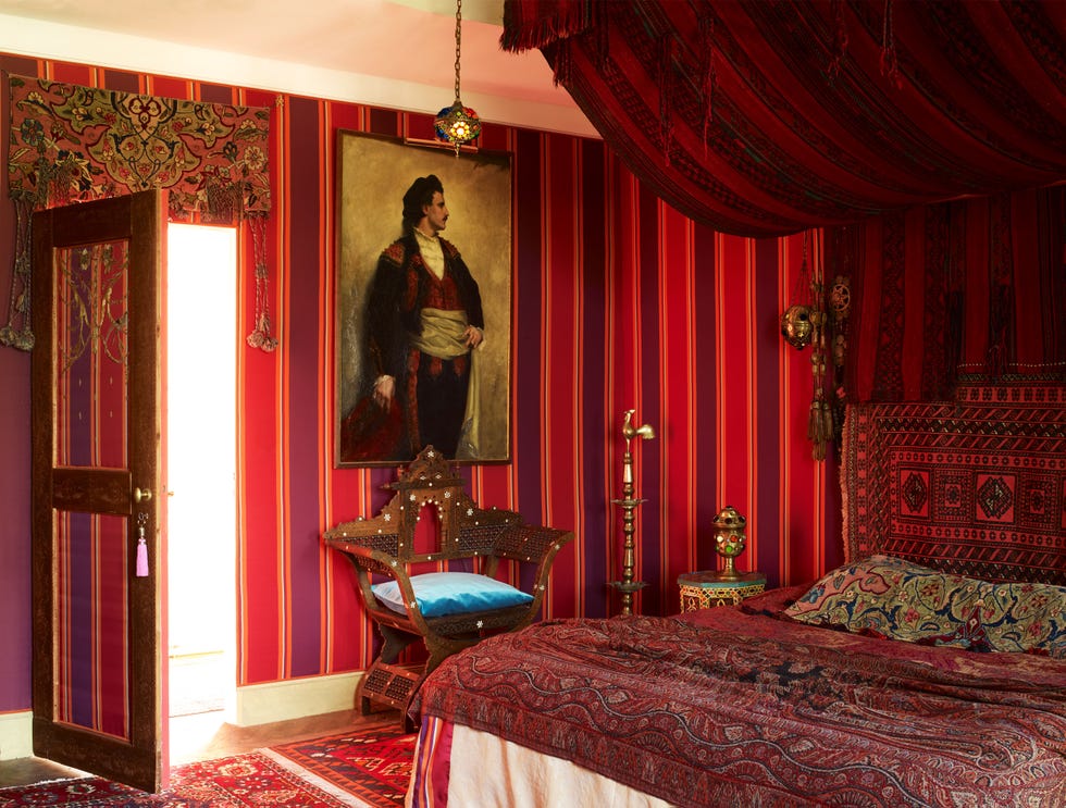 a richly decorated bedroom with vibrant red striped walls and a matching hanging canopy above and ornate furnishings