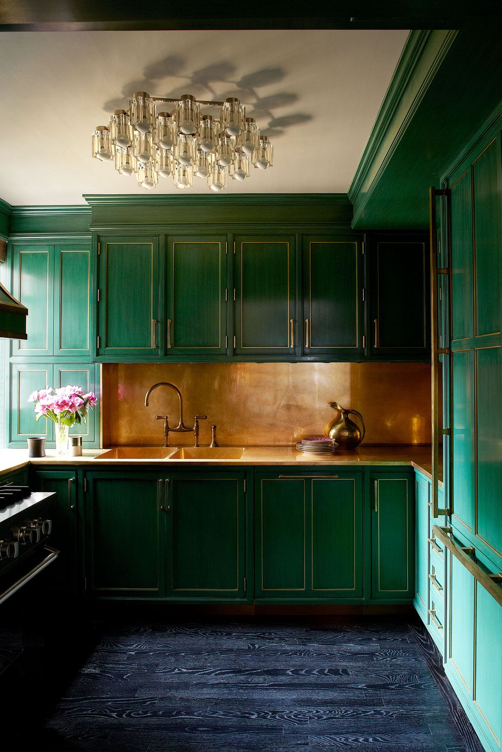 A very green galley kitchen with brass fixtures, blue wood floor, and gold tile backsplash