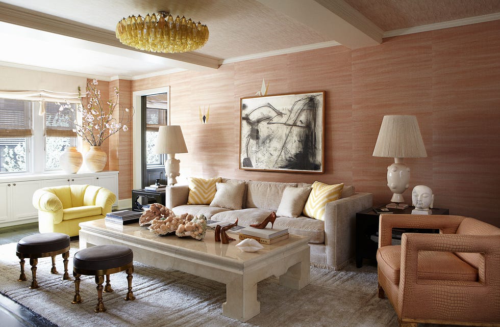 pink wallcovered spacious living room with a linen colored sofa and one open cut pink armchair and one yellow tufted side chair and blocky light colored marble like cocktail table and two small leather topped ornamental stools