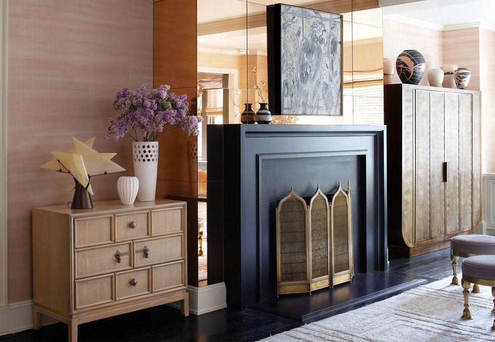 black fireplace with minaret shaped tops against a mirrored wall and next to a tall cabinet on one side and short chest on the other