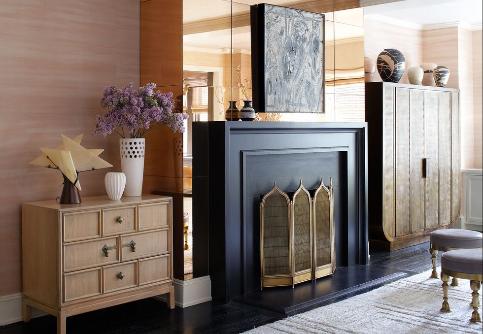 Black fireplace with minaret-shaped tops against a mirrored wall and adjacent to a tall cabinet on one side and a short cabinet on the other.