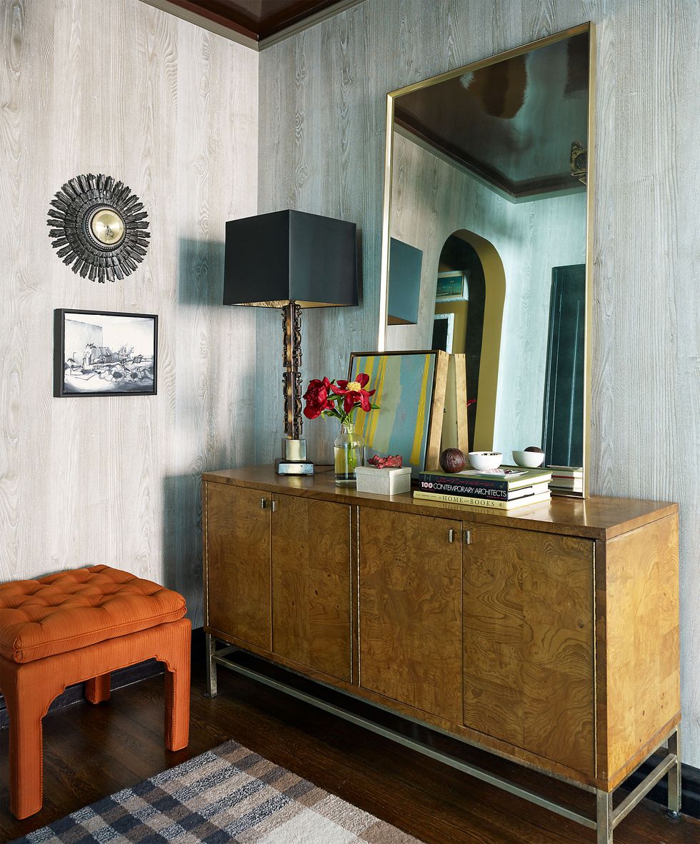 a room with a mirror standing up against the wall perched on a console and a low tufted orange stool