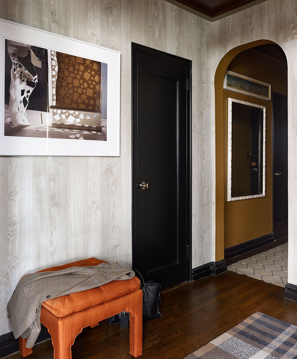 inside entryway with black door and dark wood stained floor and a small orange upholstered bench with a suit jacket draped over it and an abstract framed artwork above it on the wall