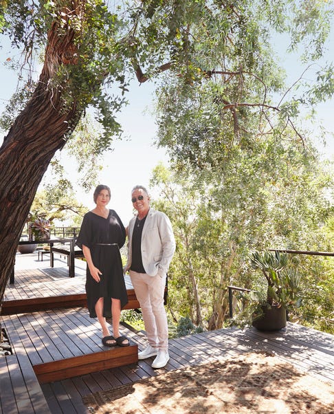 two individuals standing on a wooden deck surrounded by greenery