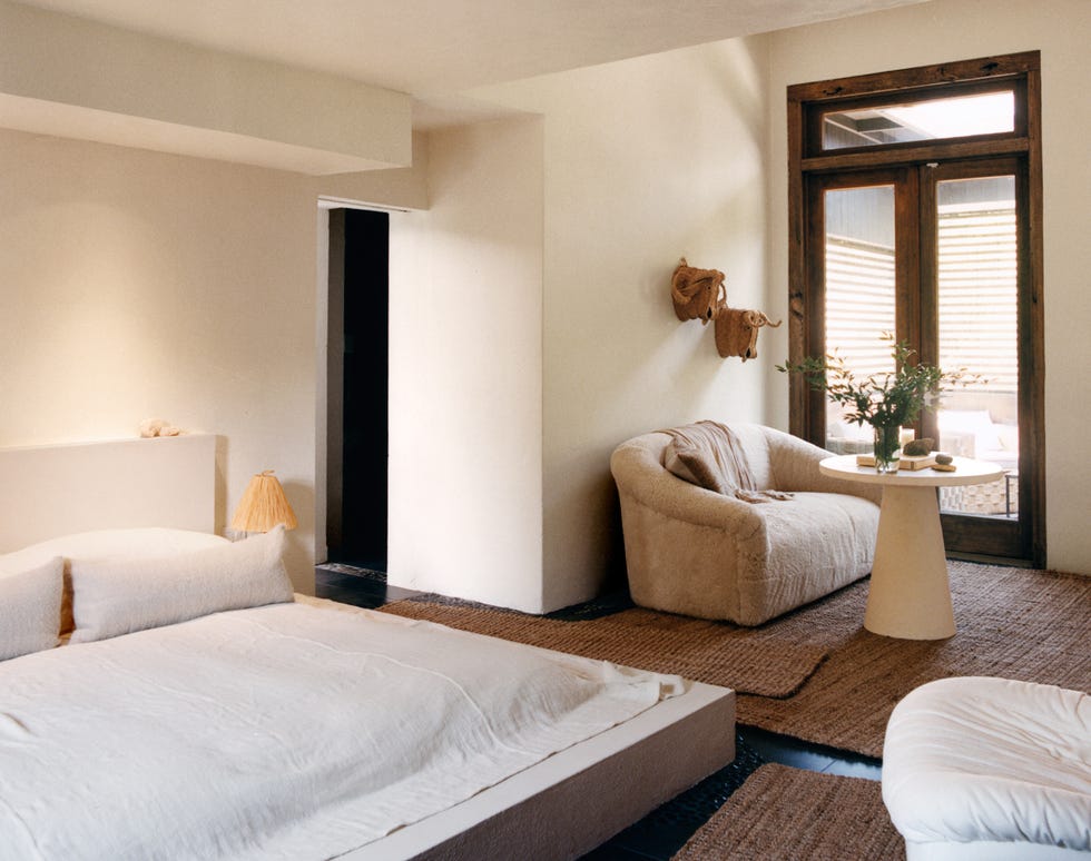 bed topped with off white and beige linens, sofa seating, and doors leading outside