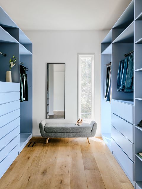 light blue closets and open shelving in a light wash wood floor and a small gray settee with a pair of pink pumps on them and a skinny window behind it and a complementary skinny mirror next to that