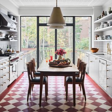 long kitchen with white cabinets and a red and white diagonal check floor with a long wooden table with chairs pulled up to it