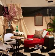 room with black and white zigzag rug and a fringed red velvet chaise a big drape from ceiling and a small pedestal table with modern white chairs